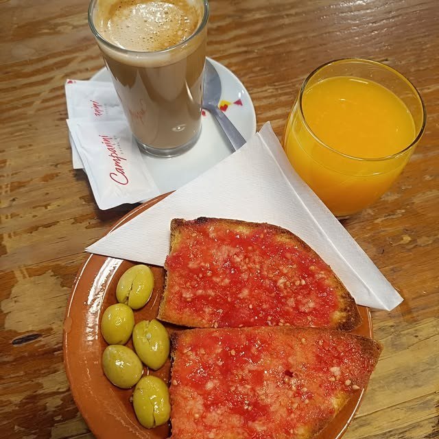 Desayuno con tostadas de tomate, aceitunas, café con leche y zumo de naranja natural